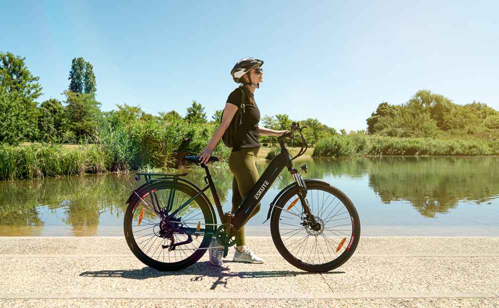 a lady with a helmet standing besides the lake with her electric trekking bikes
