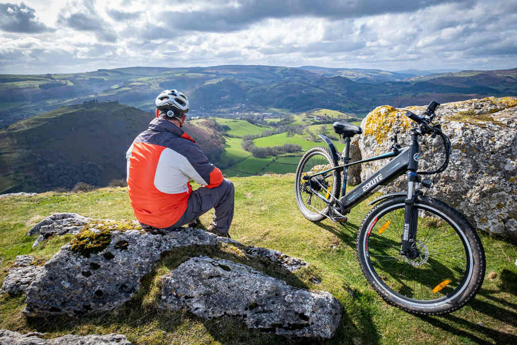 the rider sits on the rock for rest after arrive at the mountain top by electric mountain bike