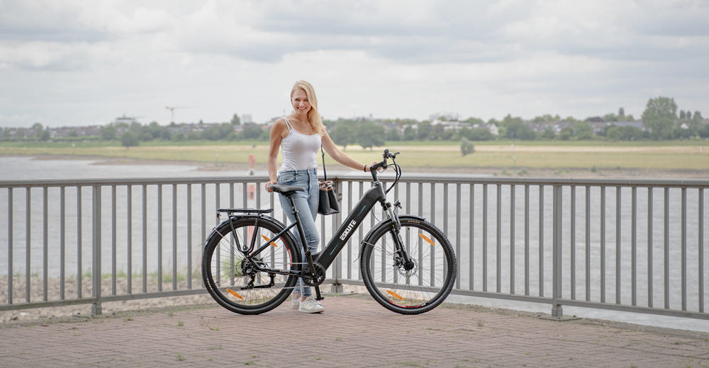 a young lady stands besides her ebike near the fence